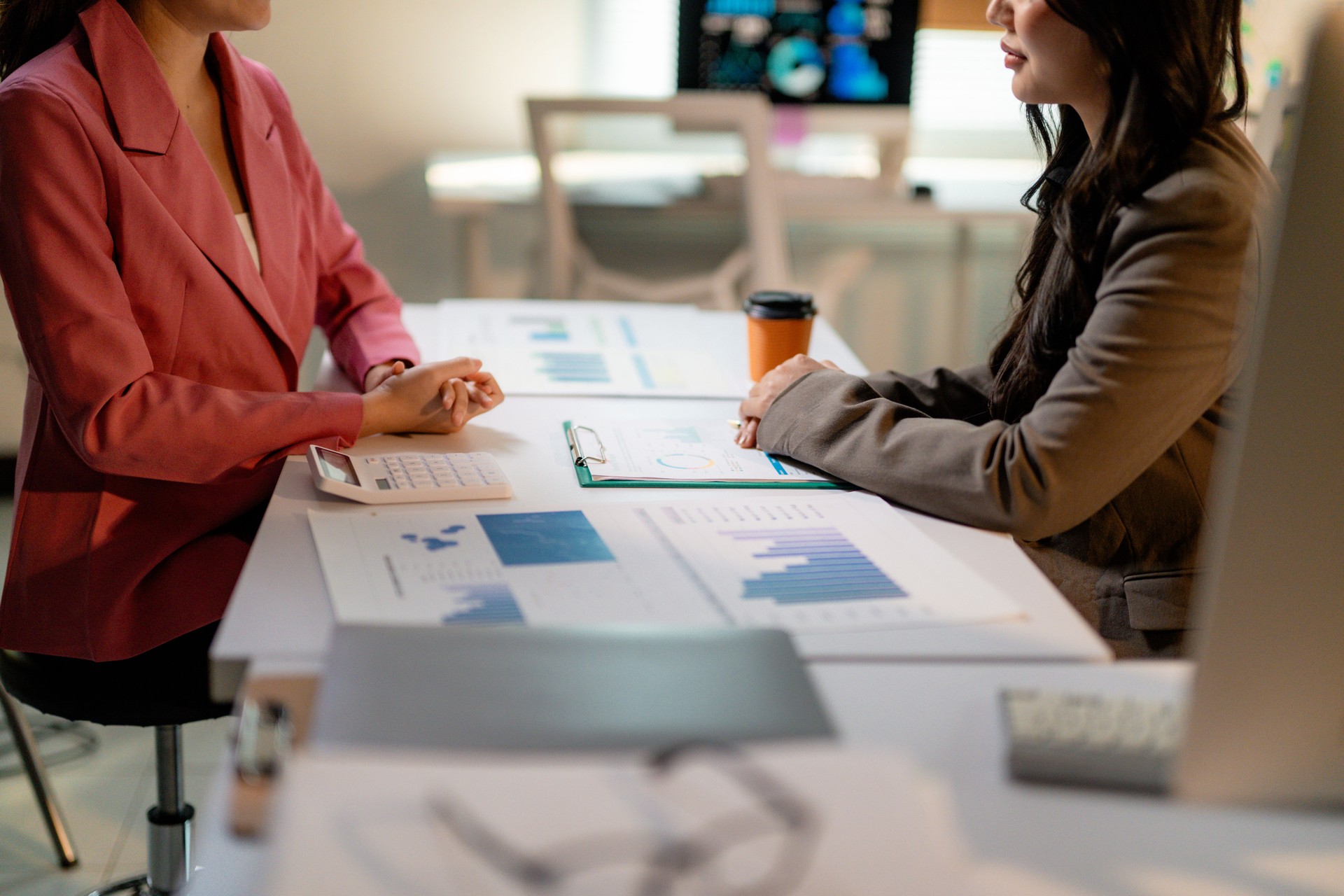 Two businesswomen are examining financial charts and discussing data during a meeting in a modern office